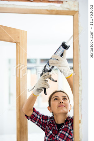 Woman herself installs a wooden door in the room - fills gaps with mounting foam Woman herself installs a wooden door in the room - fills gaps with mounting foam 111763652