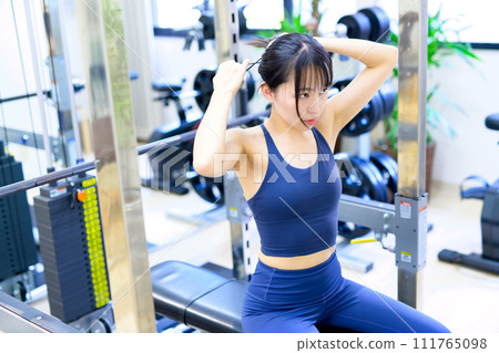 Woman tying her hair to train her body at the gym, barbell bench press, cool muscle training girl working out 111765098