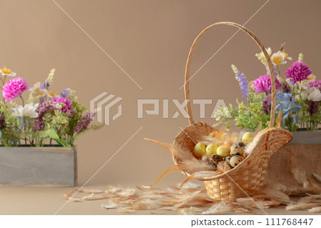 Easter composition with eggs, feathers, and spring flowers on a beige background. 111768447