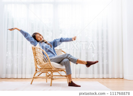 Young Asian Woman Relaxing in Modern Wicker Chair Near Window with Sheer Curtain Young Asian Woman Relaxing in Modern Wicker Chair Near Window with Sheer Curtain 111768878