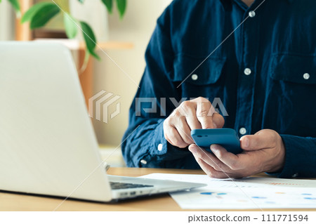 Hands of a man operating a computer and smartphone 111771594