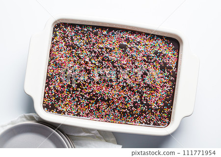 Classic chocolate cake with colored sprinkles in baking dish. Classic chocolate cake with colored sprinkles in baking dish. 111771954