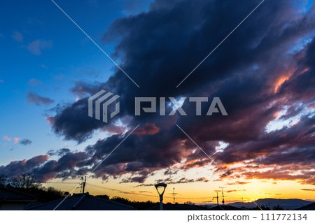 Sunset sky illuminating a residential area in early spring. Gradation of sunset clouds and blue sky floating in the golden sky. Sunset sky over Mt. Ikoma. 111772134