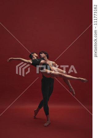 Beautiful, elegant young woman and handsome man, ballet dancer dancing against red background. Black and red 111773162