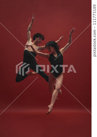 Young man and woman, ballet dancers in black cloths dancing, performing against red background 111773189