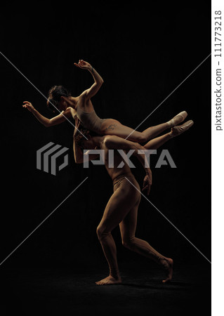 Young man and woman, ballet dancers making creative, beautiful performance, dancing against black background. 111773218