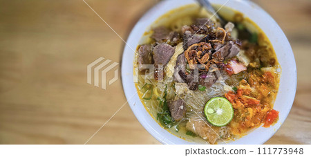 Indonesian style beef noodle soup called soto mie, freshly made soup with vermicelli rice noodle, fried shallots, chilli paste, and fried rissoles 111773948