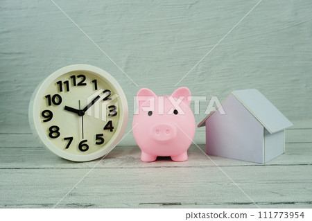 Piggy bank with house model and white clock on wooden backgroun, business background Piggy bank with house model and white clock on wooden backgroun, business background 111773954