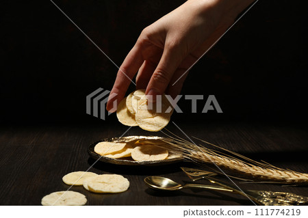 Bread in hand, spikelet and cutlery on dark background, close up 111774219
