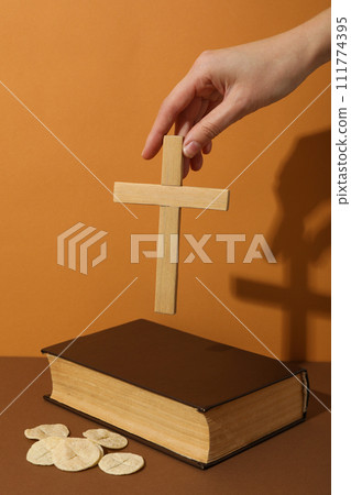 Bread, wooden cross in hand and Bible on orange background 111774395