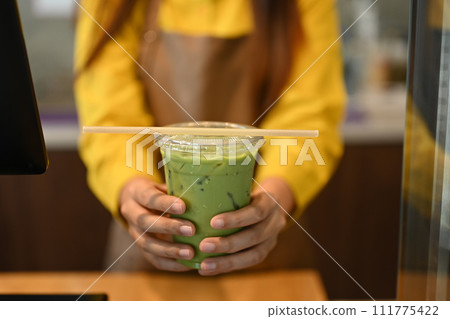 Waitress serving iced green tea late with paper straw to customer at cafe 111775422
