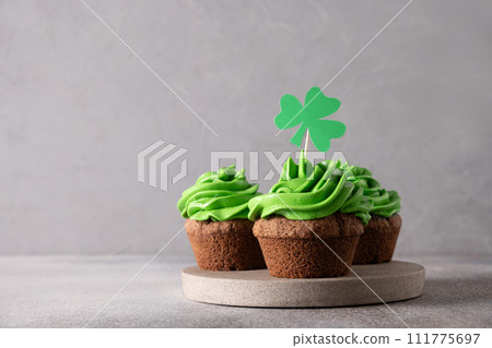 St. Patrick's Day tasty three homemade cupcakes with green whipped cream decorated shamrock and clover on gray background. Copy space. Close up. 111775697
