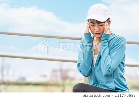 Asian woman in sportswear suffering from headache/migraine while running/walking Asian woman in sportswear suffering from headache/migraine while running/walking 111776682