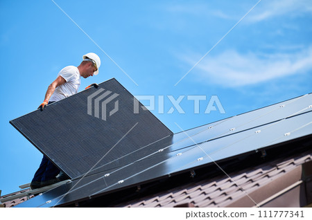 Workers building solar panel system on rooftop of house. Two men installers in helmets installing photovoltaic solar module outdoors. Alternative, green and renewable energy generation concept. 111777341