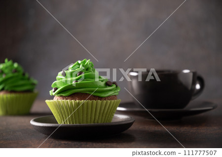 St. Patrick's Day irish coffee and chocolate cupcakes with green cream on brown background. St. Patrick's Day irish coffee and chocolate cupcakes with green cream on brown background. 111777507
