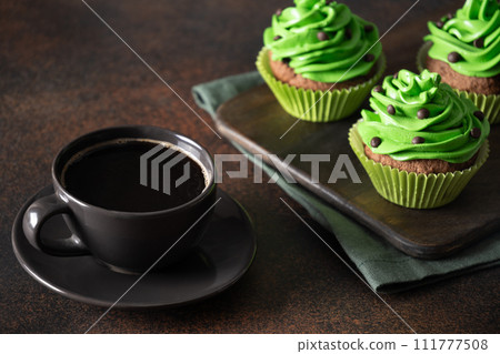 St. Patrick's Day coffee and homemade cupcakes with green whipped cream and chocolate sprinkles on brown background. St. Patrick's Day coffee and homemade cupcakes with green whipped cream and chocolate sprinkles on brown background. 111777508