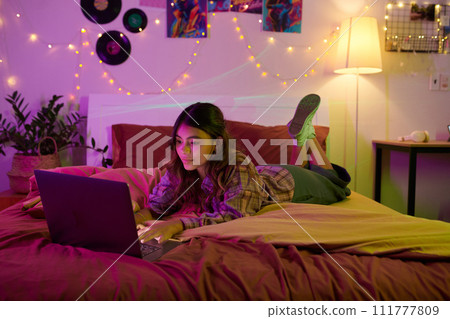 Girl resting on bed and browsing internet late at night 111777809