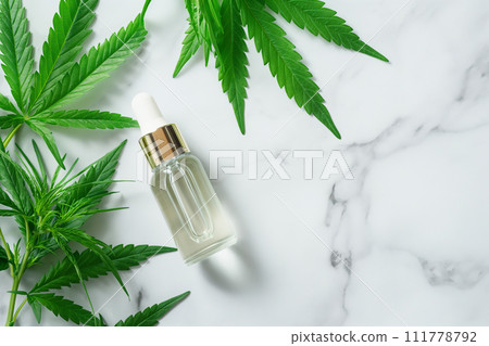 CBD Hemp oil in a dropper bottle. Cannabis oil with Marijuana plants around. Medical marijuana green leaves, alternative medicine. Oil extracts in a bottle, natural treatment, cosmetic component. 111778792