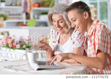 Happy senior woman with her grandson using tablet at home 111779276