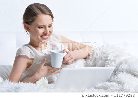 Young woman relaxing in bed, using laptop Young woman relaxing in bed, using laptop 111779288