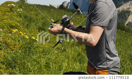 A man holds a quadrocopter in his hands, preparing it for flight. Launching a drone on a mountain hike. Commercially unmanned aerial vehicle. 111779518