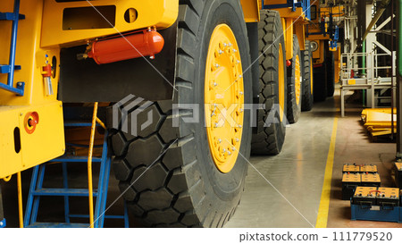Assembly line of large dump trucks. Finished dump trucks are lined up in a production shop. A close-up of the machine wheels. Production of large yellow dump trucks. Assembly line of large dump trucks. Finished dump trucks are lined up in a production shop. A close-up of the machine wheels. Production of large yellow dump trucks. 111779520