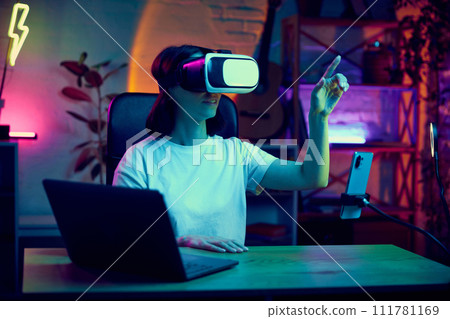 Young woman, influencer, blogger wearing VR glasses, checking modern gadgets possibilities, doing unpacking for followers 111781169