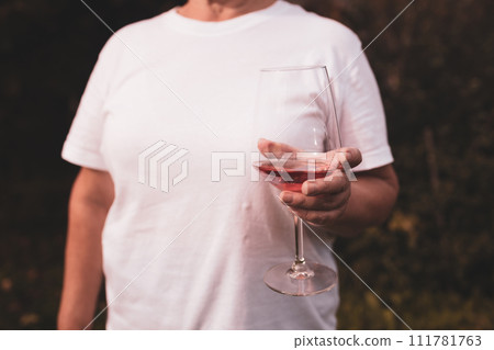 Hand holding a glass of pink wine on the blurred background at backyard, having fun outdoors. Hand holding a glass of pink wine on the blurred background at backyard, having fun outdoors. 111781763