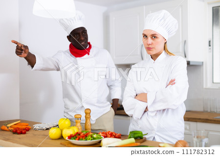 Dissatisfied adult chef controlling work of young female assistant in kitchen Dissatisfied adult chef controlling work of young female assistant in kitchen 111782312