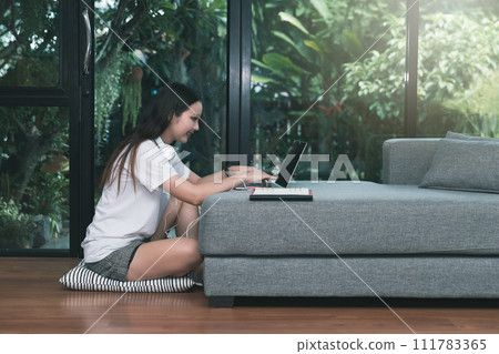 Beautiful asian woman smiling and looking at laptop in living room. Working, Learning from home concept. Beautiful asian woman smiling and looking at laptop in living room. Working, Learning from home concept. 111783365
