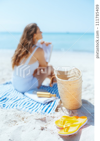 relaxed modern female on seacoast with straw bag and book relaxed modern female on seacoast with straw bag and book 111785409