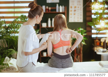 female therapist checking back condition during checkup 111785577