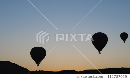 Silhouettes of hot air balloons over the mountains in the sky at dawn. Cinematic image of balloon flight. Silhouettes of hot air balloons over the mountains in the sky at dawn. Cinematic image of balloon flight. 111787039