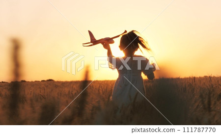 Cute little girl child running with plane toy playing at sunset sunrise wheat field happy childhood back view. Adorable female kid flying aircraft plaything pilot imagination fantasy enjoy freedom Cute little girl child running with plane toy playing at sunset sunrise wheat field happy childhood back view. Adorable female kid flying aircraft plaything pilot imagination fantasy enjoy freedom 111787770