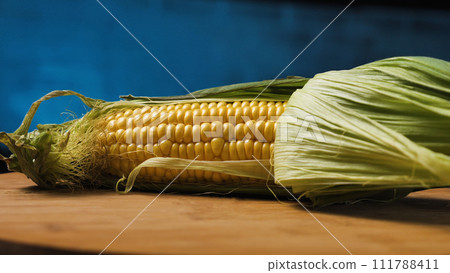 Half peeled cobs of young ripe yellow corn. Delicious fresh corn on a board. Close up. Dark blue background. Half peeled cobs of young ripe yellow corn. Delicious fresh corn on a board. Close up. Dark blue background. 111788411