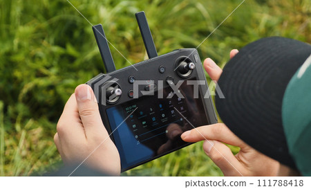 A close-up of the drone operator's hands. A man is changing settings with his finger on the screen of the quadrocopter controller. Concept of modern wireless device technology. A close-up of the drone operator's hands. A man is changing settings with his finger on the screen of the quadrocopter controller. Concept of modern wireless device technology. 111788418