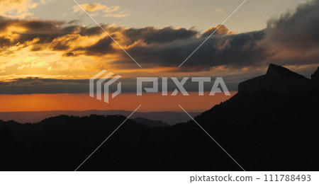 The sky at sunset looks like a layer cake. Silhouettes of mountain peaks. Layered sky, orange, yellow, blue. The beauty of the wilderness. The sky at sunset looks like a layer cake. Silhouettes of mountain peaks. Layered sky, orange, yellow, blue. The beauty of the wilderness. 111788493