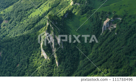 Rocks sticking out of a low forest in the mountains. Mountains covered with green grass. Beautiful majestic rock ledges on the mountainside. View from above. Rocks sticking out of a low forest in the mountains. Mountains covered with green grass. Beautiful majestic rock ledges on the mountainside. View from above. 111788496
