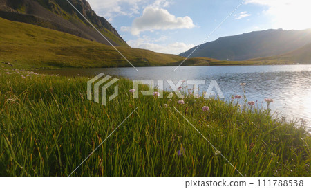 A beautiful mountain lake with ripples on the water. The mountains are covered with green grass. The morning sun shines from behind the mountain. The reflections play on the water. A beautiful mountain lake with ripples on the water. The mountains are covered with green grass. The morning sun shines from behind the mountain. The reflections play on the water. 111788538