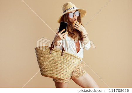 happy trendy woman in blouse and shorts taking selfie on beige 111788656