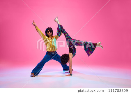 Energetic disco dance lift, couple in 1970s fashion outfit dancing in motion with playful energy against gradient pink studio background. Energetic disco dance lift, couple in 1970s fashion outfit dancing in motion with playful energy against gradient pink studio background. 111788809