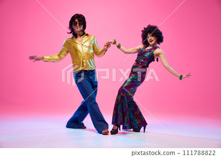 Disco Dreams. Dance duo, man and woman in retro fashion outfit dancing in motion against gradient pink studio background. Disco Dreams. Dance duo, man and woman in retro fashion outfit dancing in motion against gradient pink studio background. 111788822