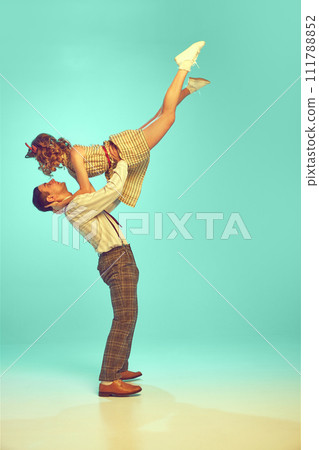Dynamic portrait of happy couple performing lively swing dance moves in motion against gradient mint background. Dynamic portrait of happy couple performing lively swing dance moves in motion against gradient mint background. 111788852