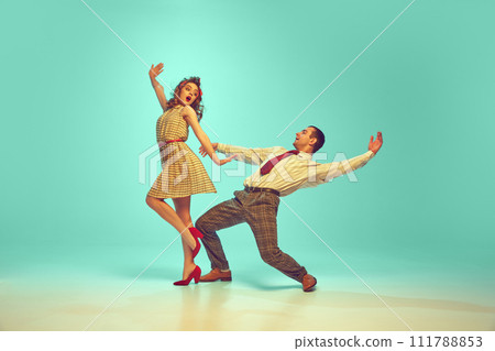 Two dancers, man and woman dressed retro outfits in mid-twirl, embodying 50s swing dance enthusiasm against gradient mint background. 111788853