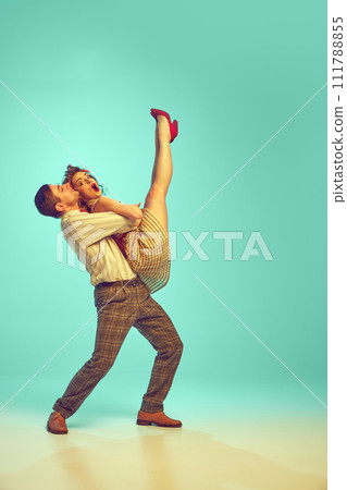 Dynamic portrait of happy couple performing lively swing dance moves in motion against gradient mint background. 111788855