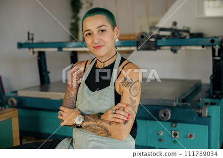 Portrait of female designer standing with crossed hands on background of print machine in workshop 111789034