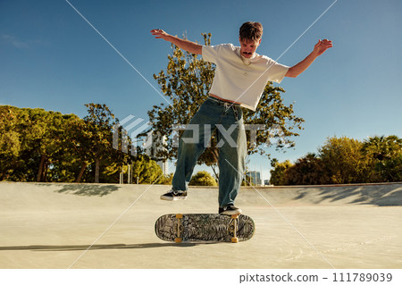 Full body of young male skater in casual outfit doing trick on skateboard riding in skate park 111789039