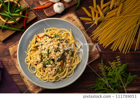Stir fried spicy spaghetti with minced chicken breast and basil leaves in white plate,Spicy pasta Pad Kra Pao.Healthy Thai fusion food.Top view 111789051