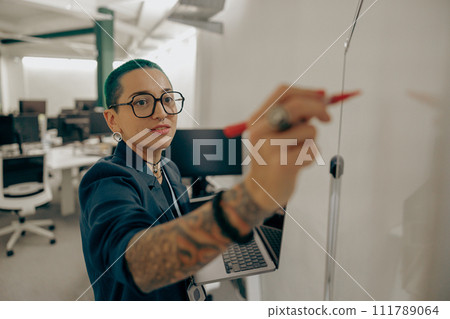 Pretty tattooed female manager is making notes on flipchart on modern coworking background Pretty tattooed female manager is making notes on flipchart on modern coworking background 111789064