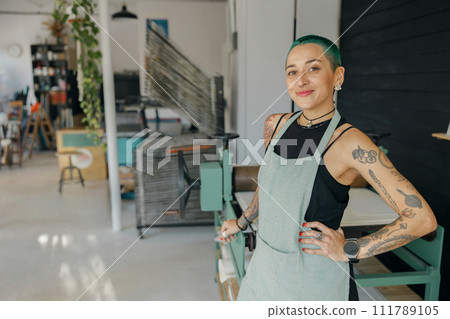 Creative female designer standing on background of workshop and looks camera with smile Creative female designer standing on background of workshop and looks camera with smile 111789105